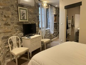 A bedroom with a stone wall, a bed, a TV, a dresser, and a chair. - CHARMING, air-conditioned house with a private, fully secured saltwater pool. (Chandolas)