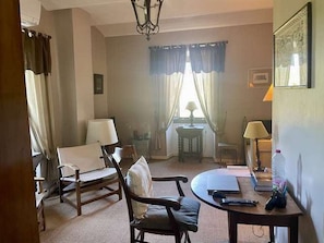 Habitació d'hotel amb sofà, una taula rodona, una làmpada i una finestra amb cortines.