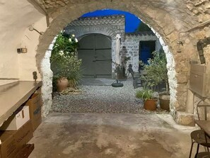 An arched stone entrance leading to a courtyard with a door, potted plants, and a table.