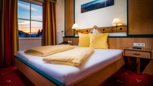 Ein Hotelzimmer mit einem Bett, zwei Nachttischlampen, einem Nachttisch, einem Fenster mit Vorhängen und einem Gemälde an der Wand.