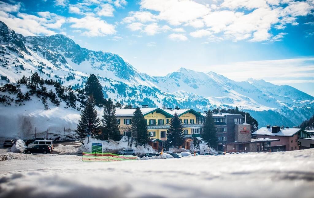 A hotel with multiple buildings, snow-covered mountains in the background, and a clear sky.