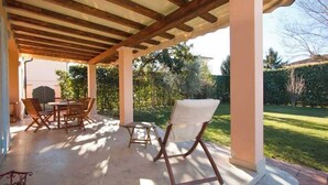 Eine Terrasse im Freien mit einer Holz-Pergola, einem Tisch mit Stühlen und Blick auf einen Garten.