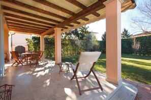 An outdoor patio with a wooden pergola, a table with chairs, and a garden view. - Villetta Angela: a villa with a garden a couple of kilometers from the sea (Pietrasanta)