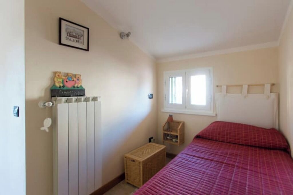 A bedroom with a bed, a radiator, a window, and a small wooden shelf.