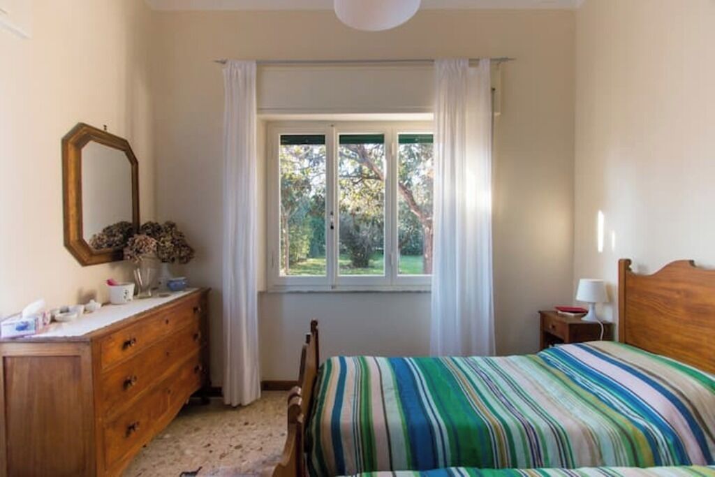 Una camera da letto con un letto, una cassettiera, uno specchio e una finestra con tende.