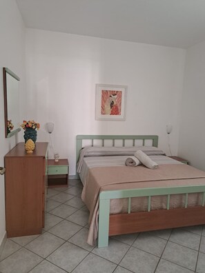 A bedroom with a bed, a dresser, a nightstand, a mirror, and a wall-mounted picture. - The Residences 2 (Marina di Modica)