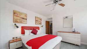 Een moderne slaapkamer met een bed, nachtkastjes, een dressoir en een plafondventilator.