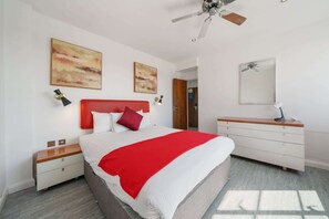 Ein modernes Schlafzimmer mit Bett, Nachttischen, einem Schminktisch und einem Deckenventilator.