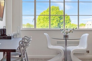 Ein stilvoller Essbereich mit Tisch und Stühlen, einem Fenster mit Blick auf Bäume und einer Vase mit Blumen.
