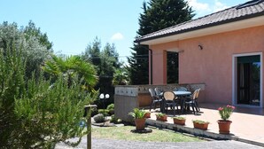Eine Terrassenfläche mit Tisch und Stühlen, umgeben von Kübelpflanzen und einem kleinen Garten.