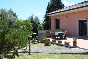 Uma área de pátio com mesa e cadeiras, cercada por vasos de plantas e um pequeno jardim.