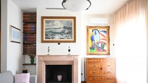 Ein Wohnzimmer mit Kamin, Bücherregalen, einer Couch und Kunstwerken an den Wänden.
