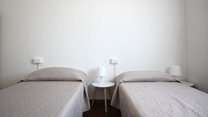 Ein Zimmer mit zwei Einzelbetten, jeweils mit Nachttisch und Lampe, sowie einer Steckdose an der Wand.