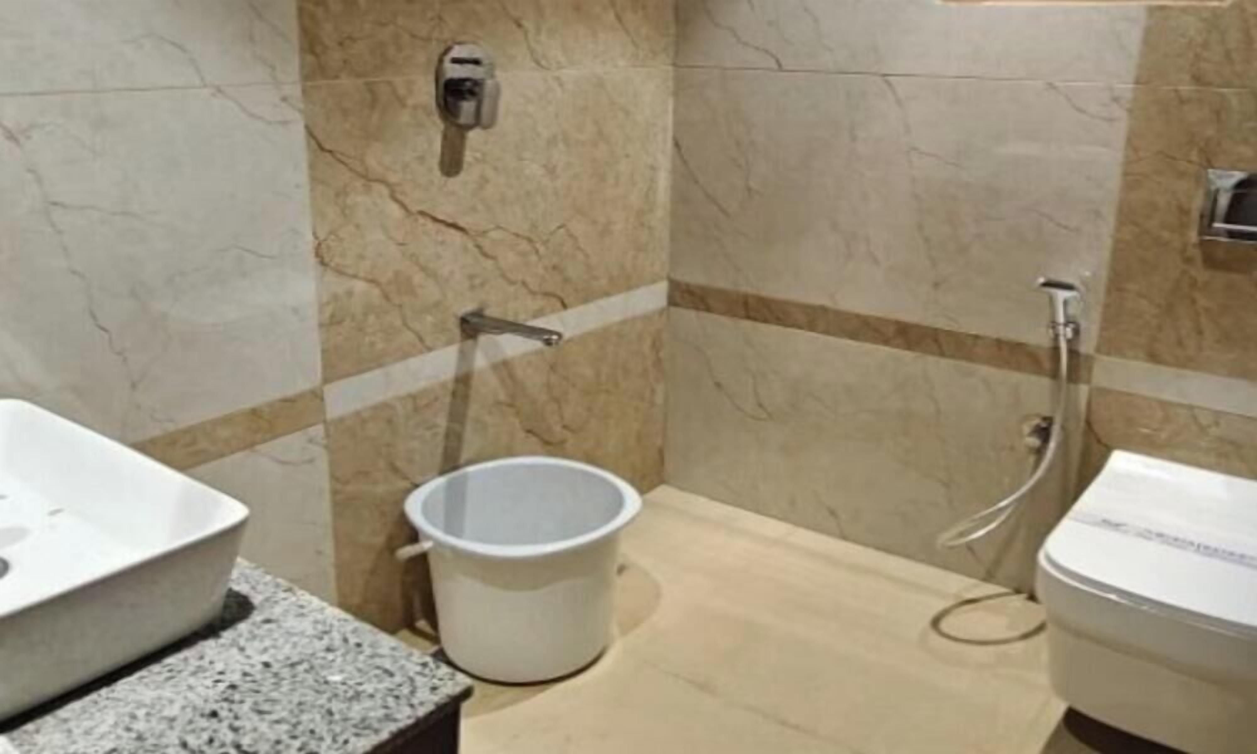 A bathroom with a sink, a bucket, a toilet, and a shower.