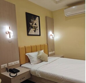 Una habitación de hotel con cama, mesitas de noche, aire acondicionado de pared y un cuadro.