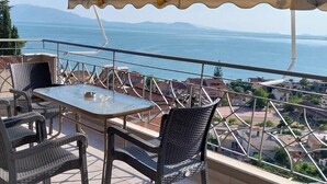 Varanda com mesa e cadeiras, oferecendo vista para a costa, com edifícios e céu claro.