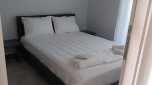 Cama bem arrumada com roupa de cama e toalhas brancas, cabeceira escura e pequena mesa de cabeceira.