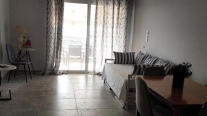 Quarto com cama, escrivaninha, cadeira, televisão e vista para o exterior.