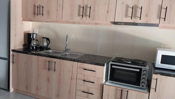 Uma cozinha com armários de madeira, bancada preta, cafeteira, pia, micro-ondas e forno elétrico.