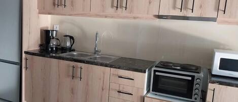 A kitchen with wooden cabinets, a black countertop, a coffee maker, a sink, a microwave, and a toaster oven.
