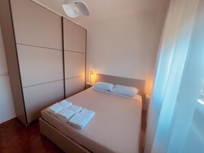 A hotel room with a bed, a bedside table with a lamp, a wardrobe, and a large window. - Da.Ma's Apartment on the Beach: Modern beachfront apartment with private garage (Giardini Naxos)