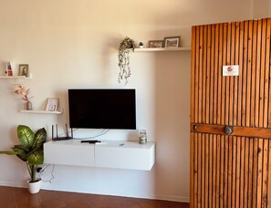 A modern living room with a flat-screen TV mounted on a white console, a potted plant, and a wooden door with a lock. - Da.Ma's Apartment on the Beach: Modern beachfront apartment with private garage (Giardini Naxos)