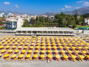 Ein Strandbereich mit vielen Sonnenschirmen und Liegestühlen, die in Reihen angeordnet sind.
