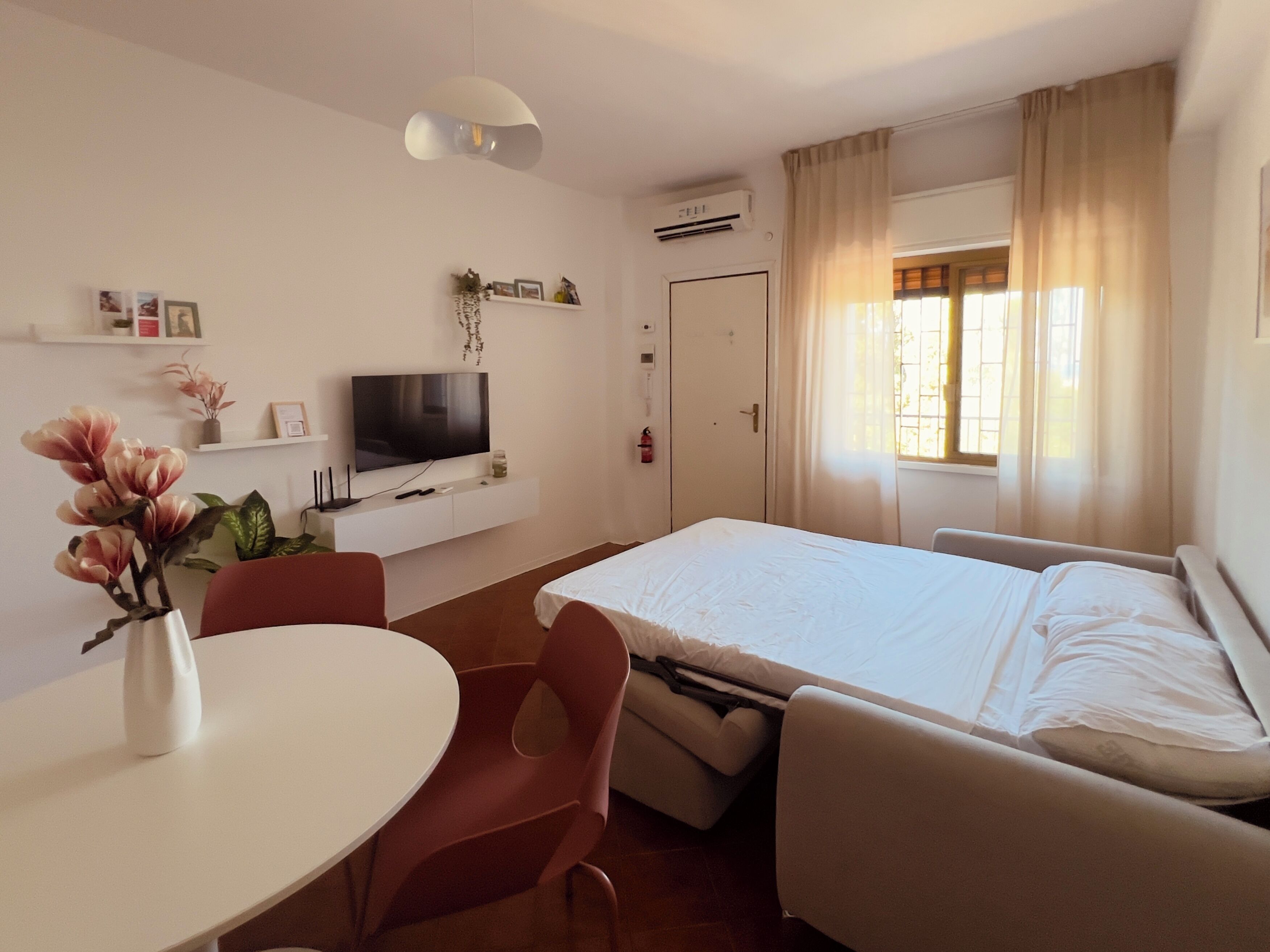 Habitación de hotel con cama, televisión, escritorio, silla y ventana con cortinas.