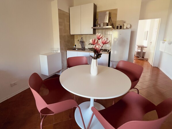 Una cucina moderna con mobili bianchi, un tavolo rotondo e sedie rosa.