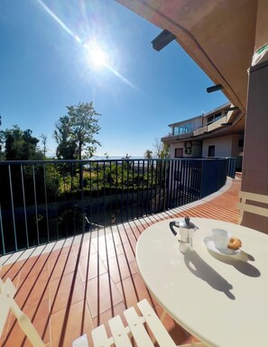 Eine Terrasse mit einem für zwei Personen gedecktem Tisch, mit Blick auf ein Gewässer und ein Gebäude.