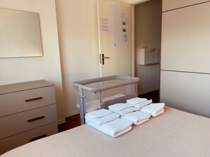 Ein Hotelzimmer mit Reisebett, einem Bett mit gefalteten Handtüchern, einem Schminktisch und einer Wand mit Kalender.