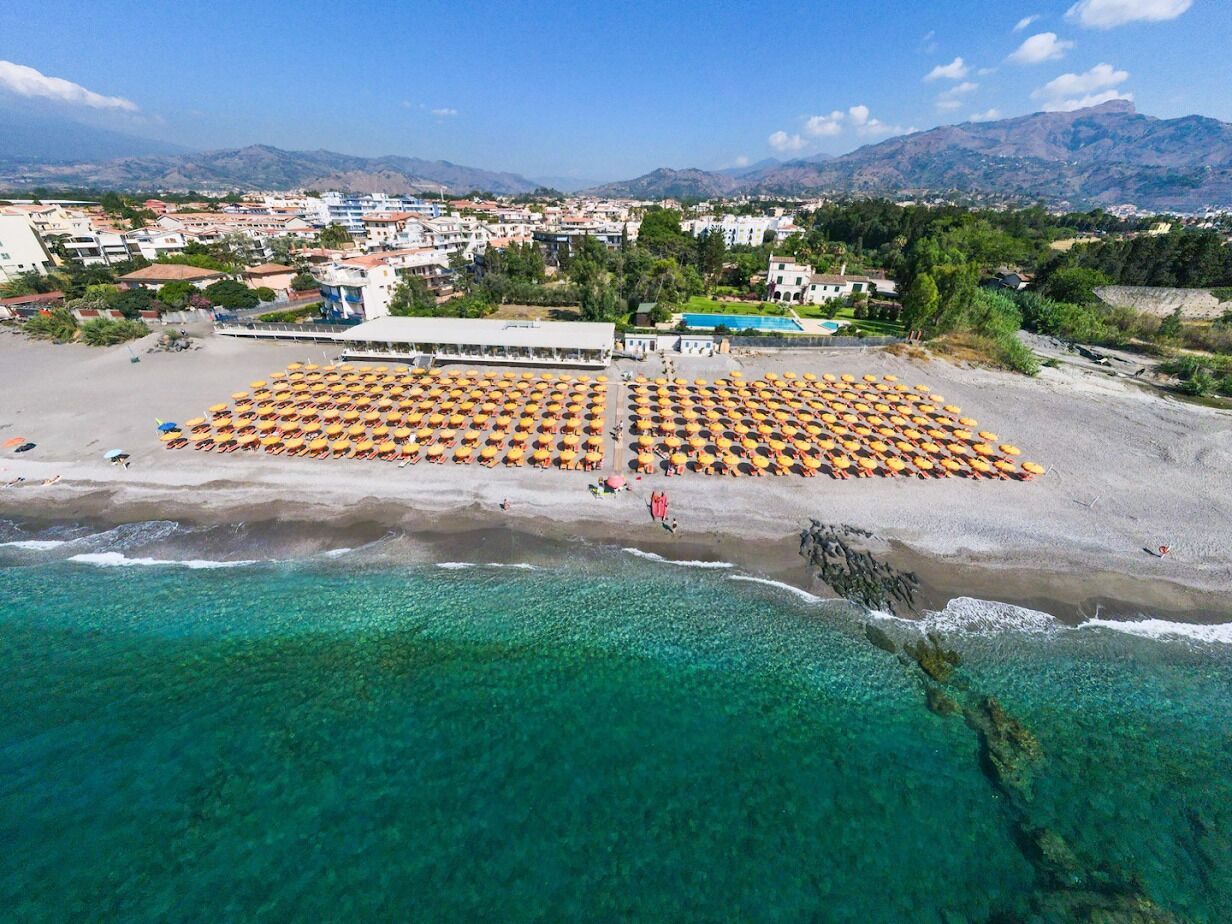 Une vue aérienne d’une plage, avec des rangées de transats et un bâtiment en arrière-plan.