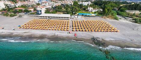 Une vue aérienne d’une plage, avec des rangées de transats et un bâtiment en arrière-plan.