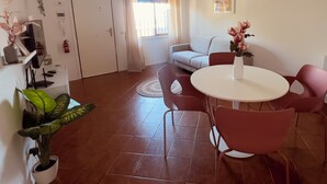 En moderne stue med spiseplads, der indeholder en sofa, et rundt bord med stole og potteplanter.