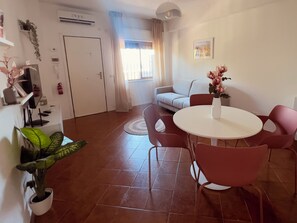 Ein modernes Wohnzimmer mit Essbereich, ausgestattet mit einer Couch, einem runden Tisch mit Stühlen und Topfpflanzen.