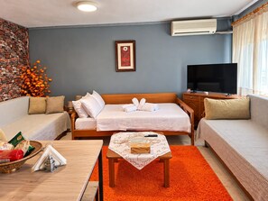 A hotel room with a bed, two sofas, a TV, and a small table with a tray. - Aegean Sea & Mount Olympus View Guesthouse (Palaio Eleftherochori)