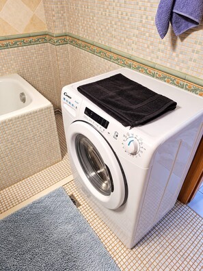 Un lave-linge à chargement frontal doté d’un panneau de commande, d’une cuve blanche et d’un pare-éclaboussures en carreaux décoratifs.