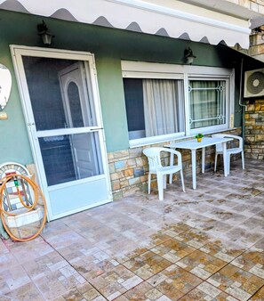 Un espace patio avec une table et des chaises, un tuyau d’arrosage et une porte.