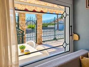 Ein Zimmer mit Blick auf einen eingezäunten Außenbereich, ein Fenster mit Vorhang und ein kleiner Tisch mit Pflanze und einem gelben Gegenstand.