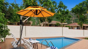 Area piscina con lettini, un tavolo con bevande e un ombrellone.