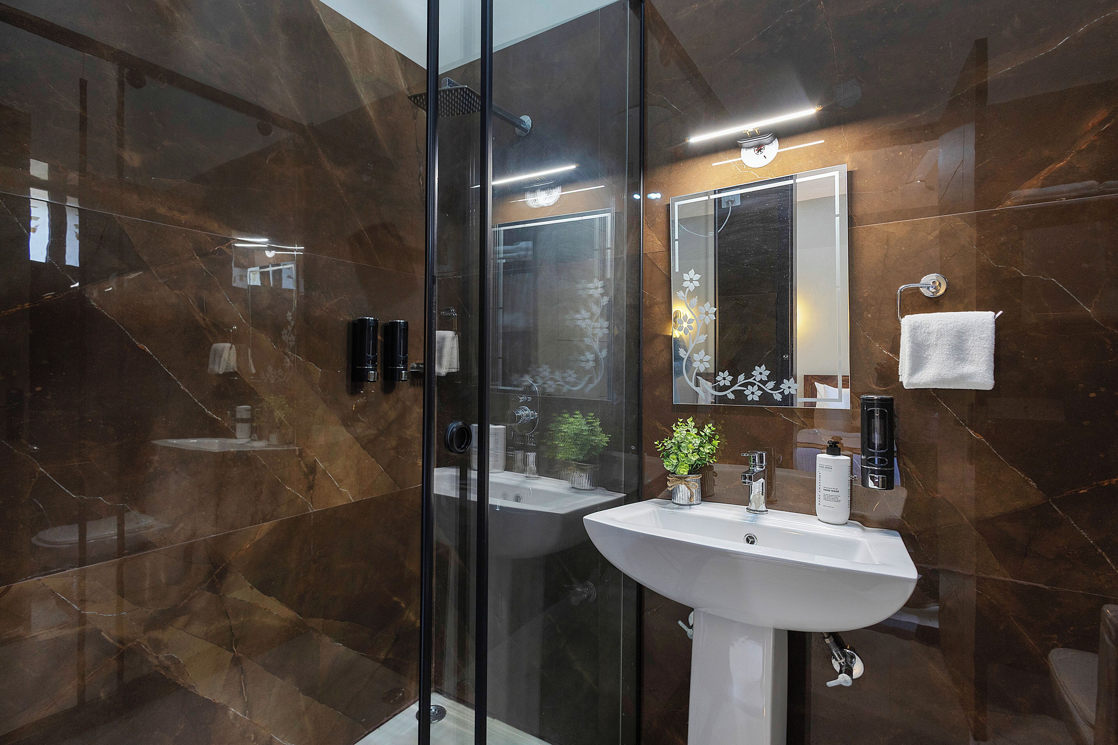 Un baño moderno con ducha envuelta en vidrio, un lavamanos blanco y un espejo grande.