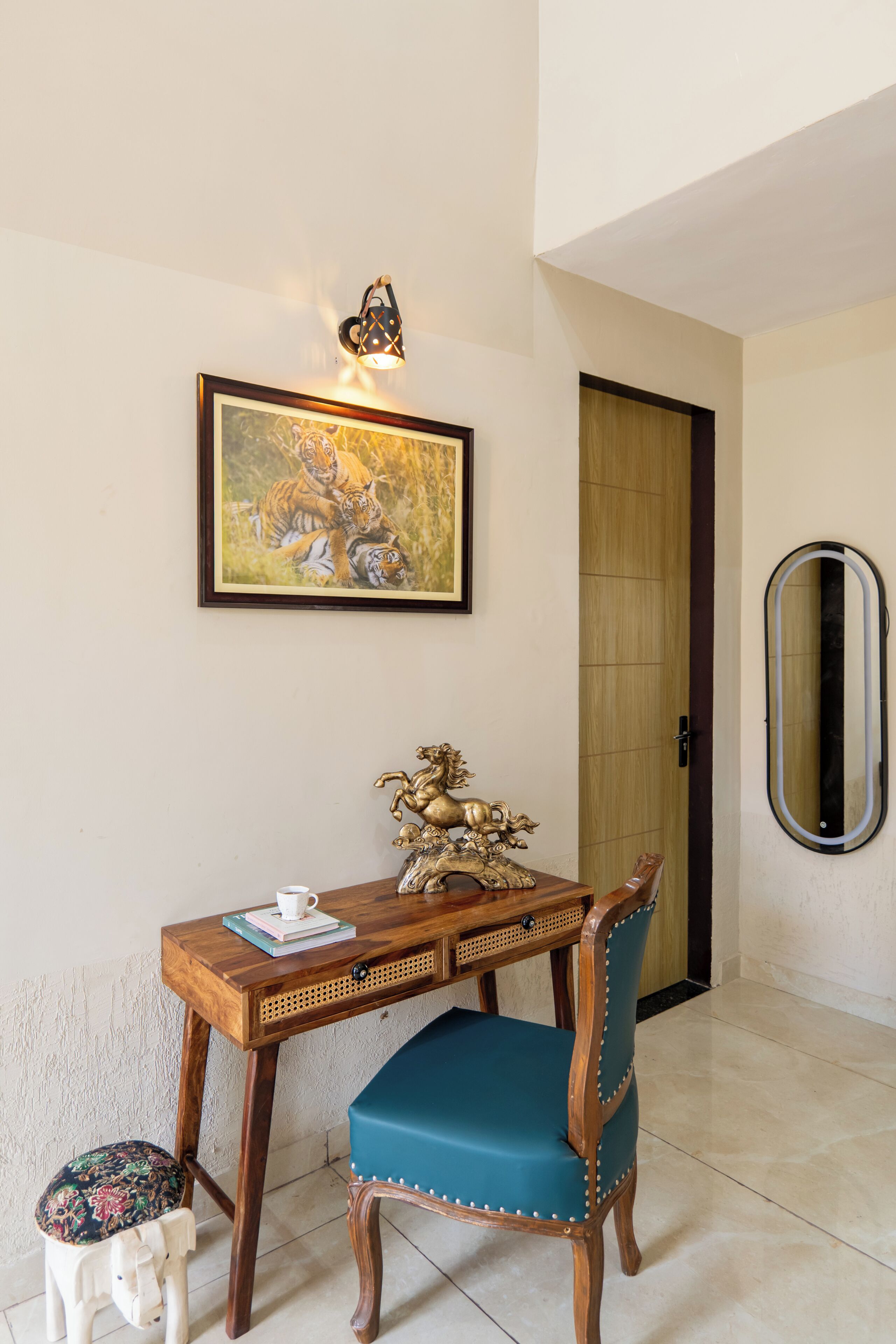 A room with a wooden desk, a blue chair, a framed painting of tigers, a decorative horse sculpture, and a mirror on the wall.