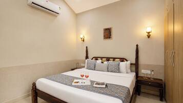 A hotel room with a bed, bedside tables, an air conditioning unit, and wall-mounted lighting.