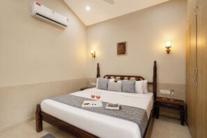 A hotel room with a bed, bedside tables, an air conditioning unit, and wall-mounted lighting.