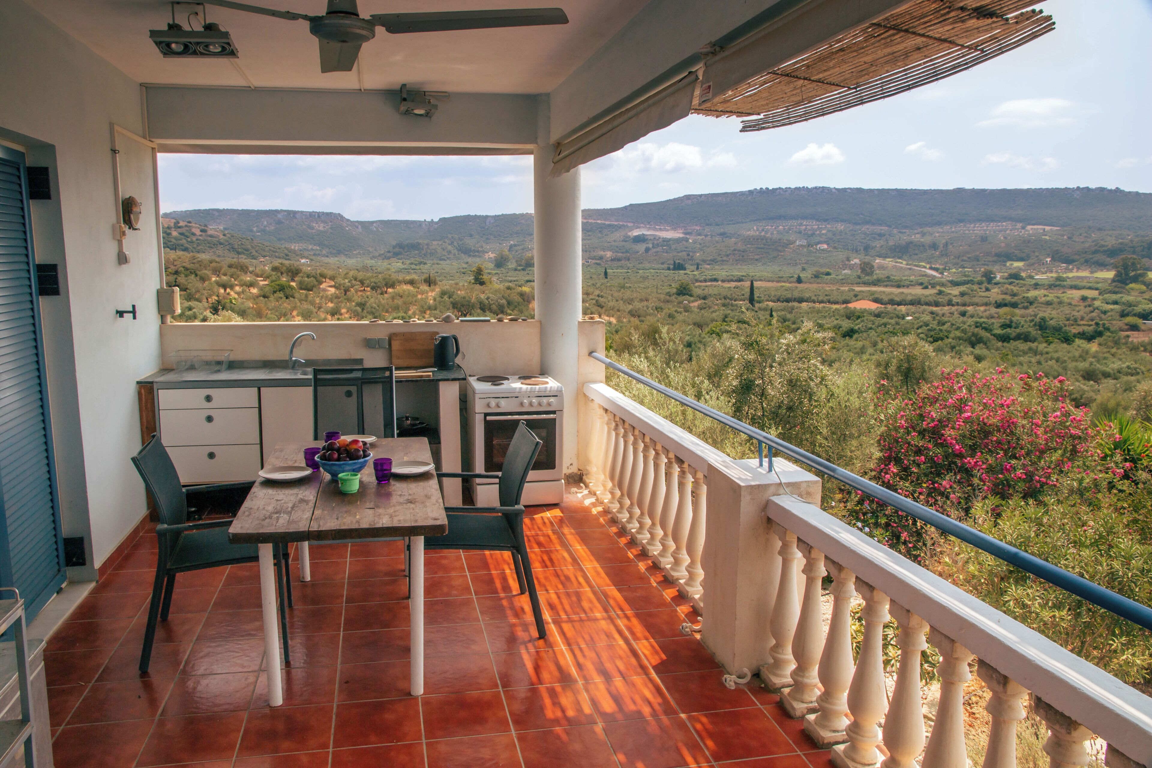 A balcony with a kitchen area, including a table, chairs, and a view of the countryside.