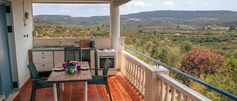 Ein Balkon mit Küchenzeile, inklusive Tisch, Stühlen und Blick ins Grüne.