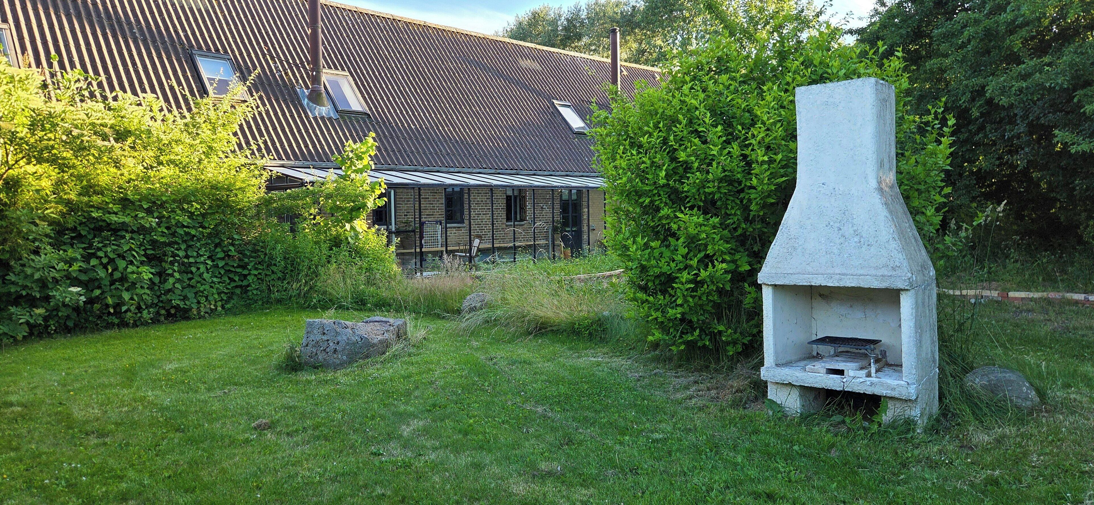 A stone-built outdoor grill structure in a grassy area with a house in the background.