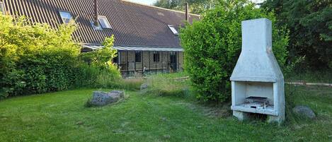 A stone-built outdoor grill structure in a grassy area with a house in the background.