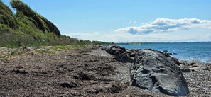 A rocky shoreline with a clear view of the sea and distant land. - Views across the fields to the sea on Langeland (Tranekær)