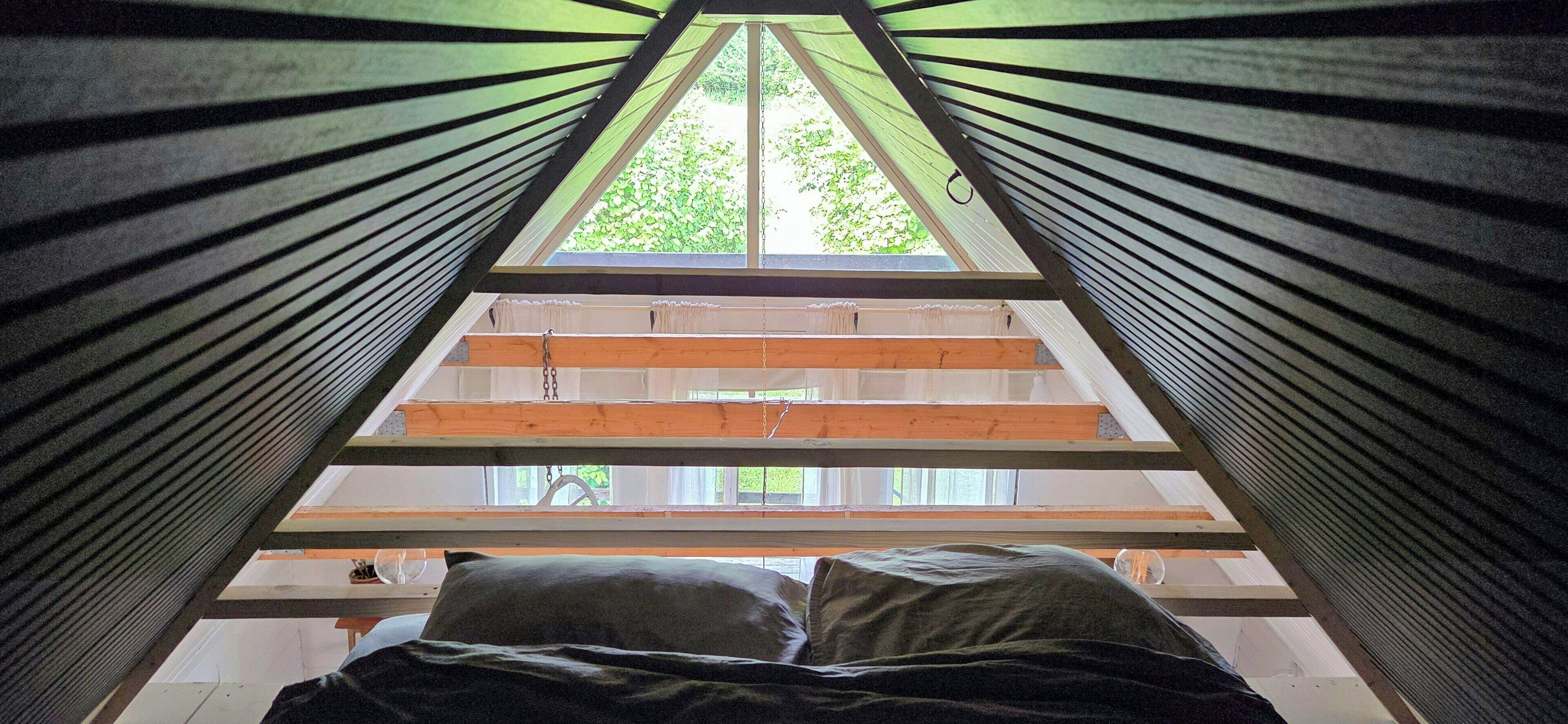 Una habitación con techo inclinado, una cama con almohadas y vistas al verdor exterior.